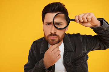 Man looking through magnifier glass on yellow background