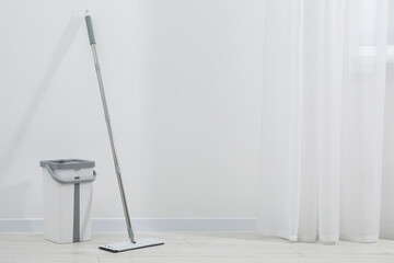 Mop and plastic bucket indoors. Space for text