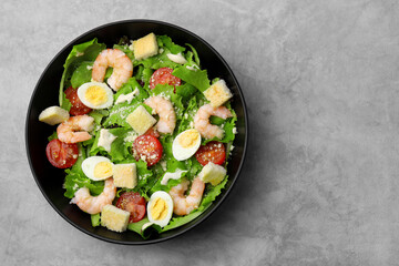 Delicious Caesar salad with shrimps on grey table, top view. Space for text