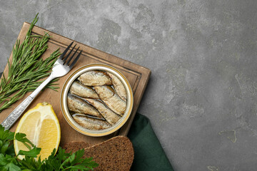 Tin can with tasty sprats served on grey textured table, flat lay. Space for text