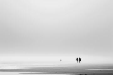 Three men stand and walk on a foggy beach.
