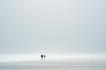 Fototapeta na wymiar Three men stand and walk on a foggy beach.