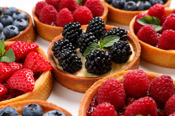 Tartlets with different fresh berries on white table, closeup. Delicious dessert