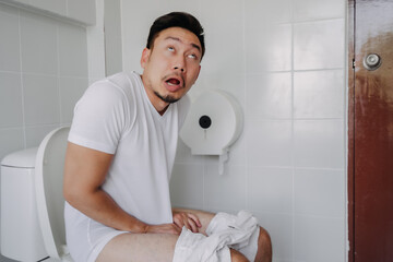 Funny face asian man pushing poop in the toilet as he has constipation. - obrazy, fototapety, plakaty