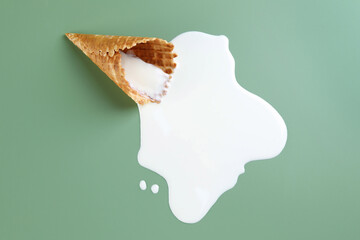 Melted ice cream and wafer cone on green background, top view