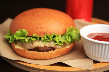 Tasty cheeseburger and sauce on wooden board, closeup