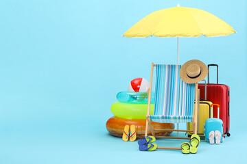 Deck chair, umbrella, suitcases and beach accessories on light blue background, space for text. Summer vacation