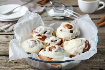 Tasty cinnamon rolls with cream on wooden table, closeup