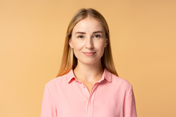 Fototapeta premium Portrait of confident attractive blonde woman wearing pink shirt looking at camera isolated on beige background