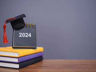 Study goals, 2024 Desk calendar with graduation hat on colorful hardcover book. The concept for Resolution, Goal, Action, Planning, and manage time to success graduate in New Year 2024