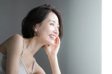 窓際を笑顔で見つめる女性のクローズアップの横顔　美容やポシティブなイメージに