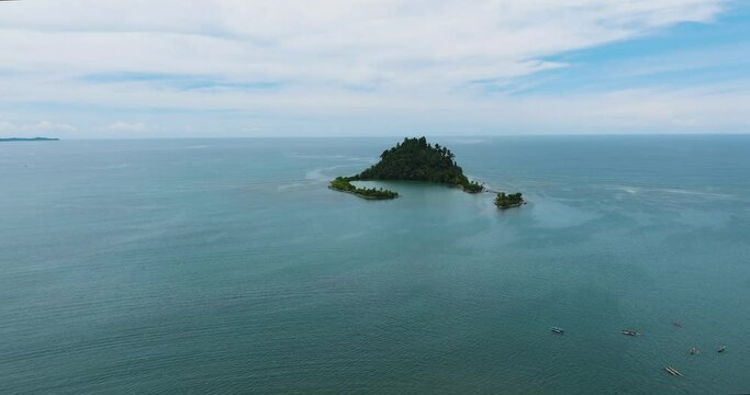 Cabugao island surrounded by calm ocean waves. Beautiful scenic of blue sea under clear sky and clouds. Davao Oriental, Philippines. Mindanao.