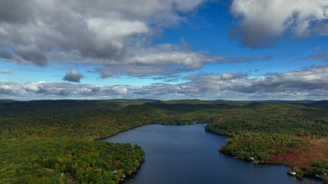 A high altitude view over Oscawana Lake in New York during the fall on a beautiful day. The camera dolly out and tilt down over the lake with the mountains in the background.