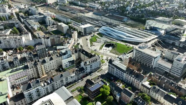 Backwards drone tilt shot of the new Rennes station between high-rise buildings.