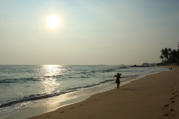 Fototapeta na wymiar Wild raw empty beach in Sri Lanka with a girl wearing red dress