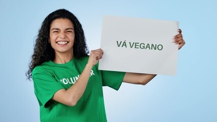 Volunteer woman, vegan board and studio for smile on face, cheers and pointing by blue background. Recruitment, diet choice and call to action for sustainable food, fist sign or poster in Barcelona