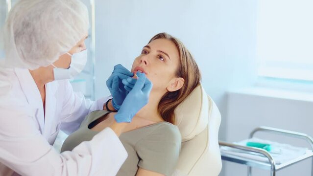 Hands of cosmetologist making filler injection in female lips. Young woman is receiving procedure with enjoy.