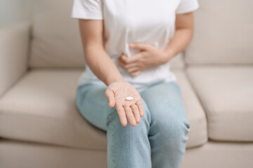 woman hand holding medicine painkiller pill and water glass on the sofa at home, taking for headaches,  stomach ache, Diarrhea Pain from food poisoning, Endometriosis, Hysterectomy and Menstrual - obrazy, fototapety, plakaty