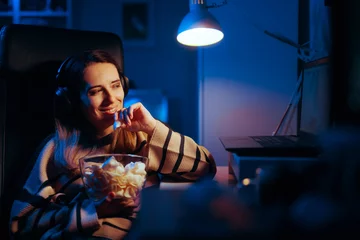 Fotobehang Happy Woman Binging a Show Eating Potatoes Chips at Night. Cheerful girl watching a movie having a late snack in front of a screen  © nicoletaionescu