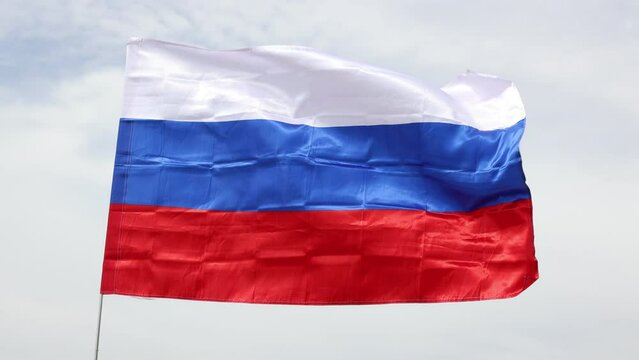 Russian tricolor flag waving in wind against sky. Russian flag on blue sky background.
