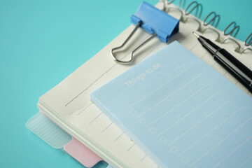 To do list in notebook with office suppliers on desk.