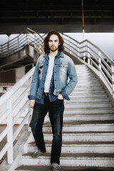 Stylish male model with long hair posing on the stairs on a summer day. Fashion and lifestyle...