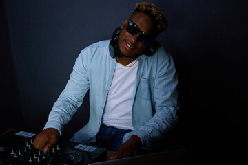 On gray background, an African American is posing at a DJ console. Popular dj in the studio behind...