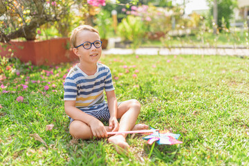 Boy in glasses is playing with pinwheel in a garden