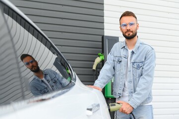 Stylish man inserts plug into the electric car charging socket