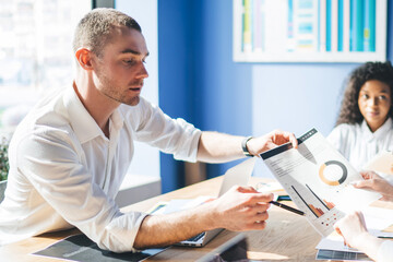 Obraz premium Elegant businessman discussing results in document with multiracial colleagues in office