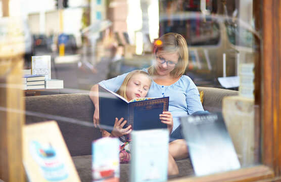 Reading, books and mother with child in bookshop window with smile, learning and relax with knowledge. Storytelling, happy mom and girl in library together with story, fantasy and education in window