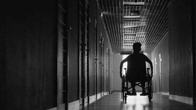 Full black and white shot of woman riding wheelchair through hospital corridor and looking around