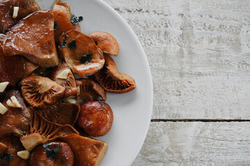 Top view white plate of mushrooms and wooden table with copyspace. Edible mushrooms Rovellons or Niscalos. 