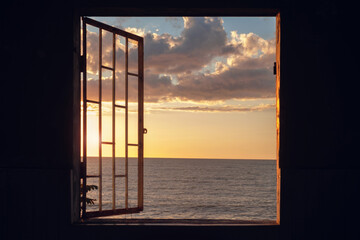 View of a sunset seascape from the window with cage in an in the dark room