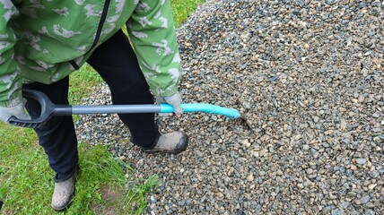 rural worker reloads with a shovel gray gravel from the ground from a pile into the box of a garden...