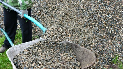 a man loads crushed stone from a large pile on the local area with a shovel into a garden wheelbarrow, loading gravel into a wheelbarrow by hand using a shovel, a villager reloads screenings