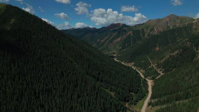 Aerial cinematic drone summer high altitude dirt road Silverton Mountain Ski Resort southern Colorado blue sky late morning stunning lush green blue sky partly cloudy Rocky Mountains forward motion
