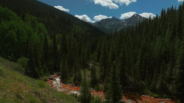 Aerial cinematic drone orange river Cement Creek summer high altitude downtown Silverton Telluride Prospect Gulch Colorado Rocky Mountains stunning drive looking up steam forward slowly movement
