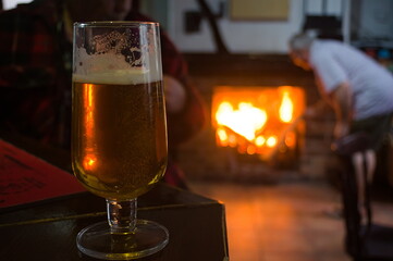 glass of beer on the table with a defocused fireplace in the background