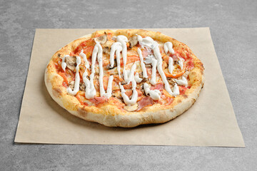 Pizza with ham, champignon and tomato slices on parchment paper