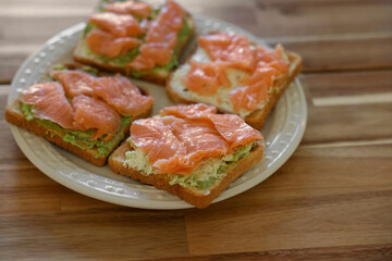 Sandwiches with avocado spread and salmon on wooden table, closeup