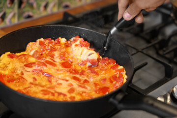 Man cooking tasty fried eggs with tomatoes on stove, closeup
