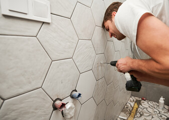 Side view of male plumber using electric drilling machine while working on home renovation. Man...