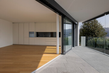 Inside a large space, a studio with a kitchen and a large window opening onto the terrace. - obrazy, fototapety, plakaty