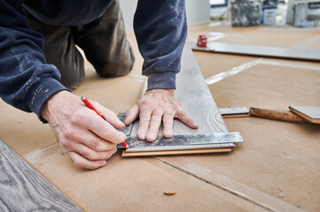 Close up of man hands using metal ruler and pencil while drawing line on laminate wooden board. Male construction worker measuring laminate panel for floor installation. Flooring renovation concept.