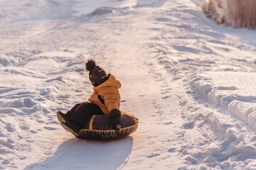 Active toddler boy in a yellow jacket sliding down the hill on snow tube.Winter fun,active...