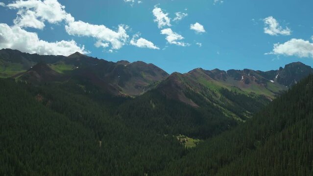 Aerial cinematic drone summer high altitude Silverton Mountain Ski Resort southern Colorado blue sky late morning stunning lush green blue sky partly cloudy Rocky Mountains upward jib motion