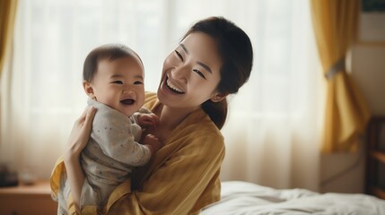 young attractive asian mother is holding his laughing baby on the chest, 16:9, copy space - obrazy, fototapety, plakaty