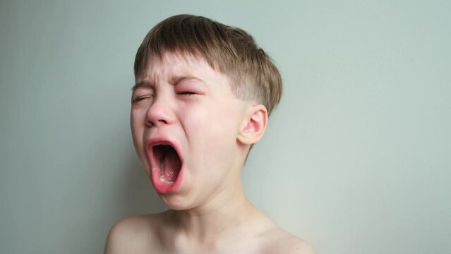 Dramatic portrait of a crying 7 year old boy. Tears flow from the eyes. The upset child. A swollen eye hurts due to a blow or insect bite. Sorrow. Children violence. Stress concept. Kids hysteria. 4K.