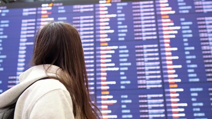 Lady in airport terminal approaches schedule of aircraft flights. Woman searches for right flight for journey and eventually finds correct plane, side view